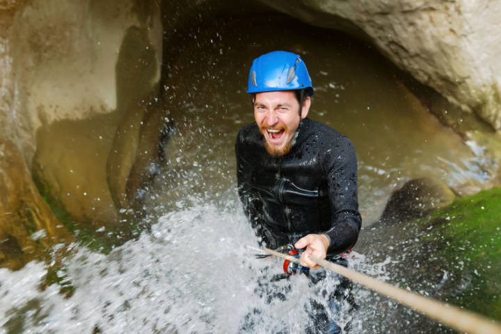 Man klettert beim Canyoning durch einen Wasserfall aus einer Schlucht heraus